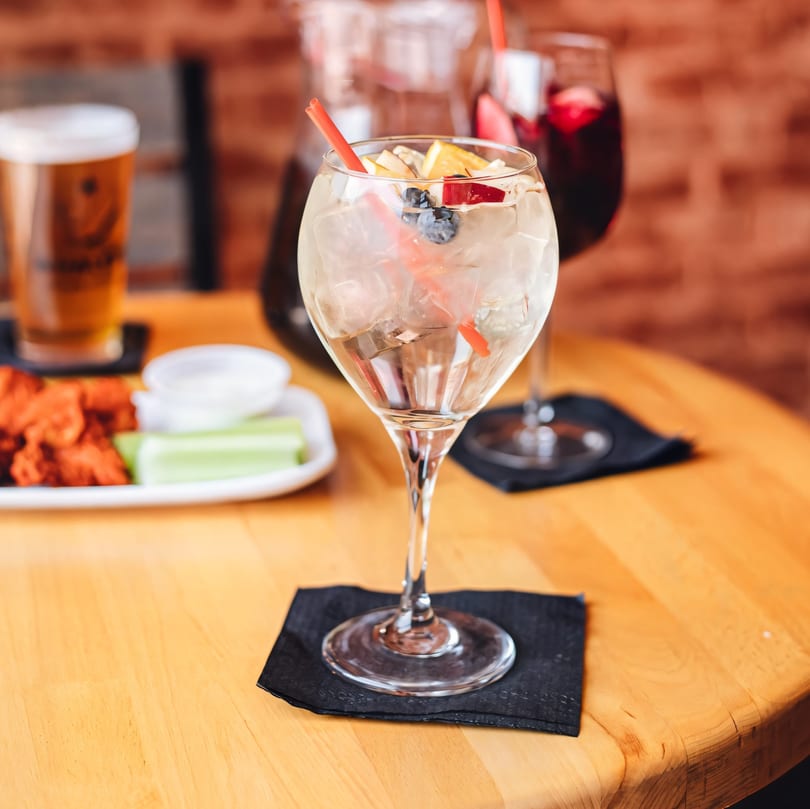 A refreshing white sangria with fruit and ice, next to a beer and chicken wings.