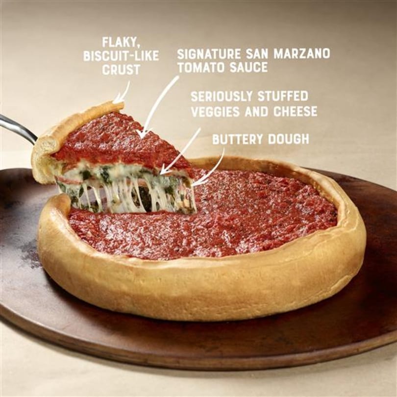 A deep-dish pizza with a slice being removed, showing gooey cheese, vegetables, and tomato sauce.